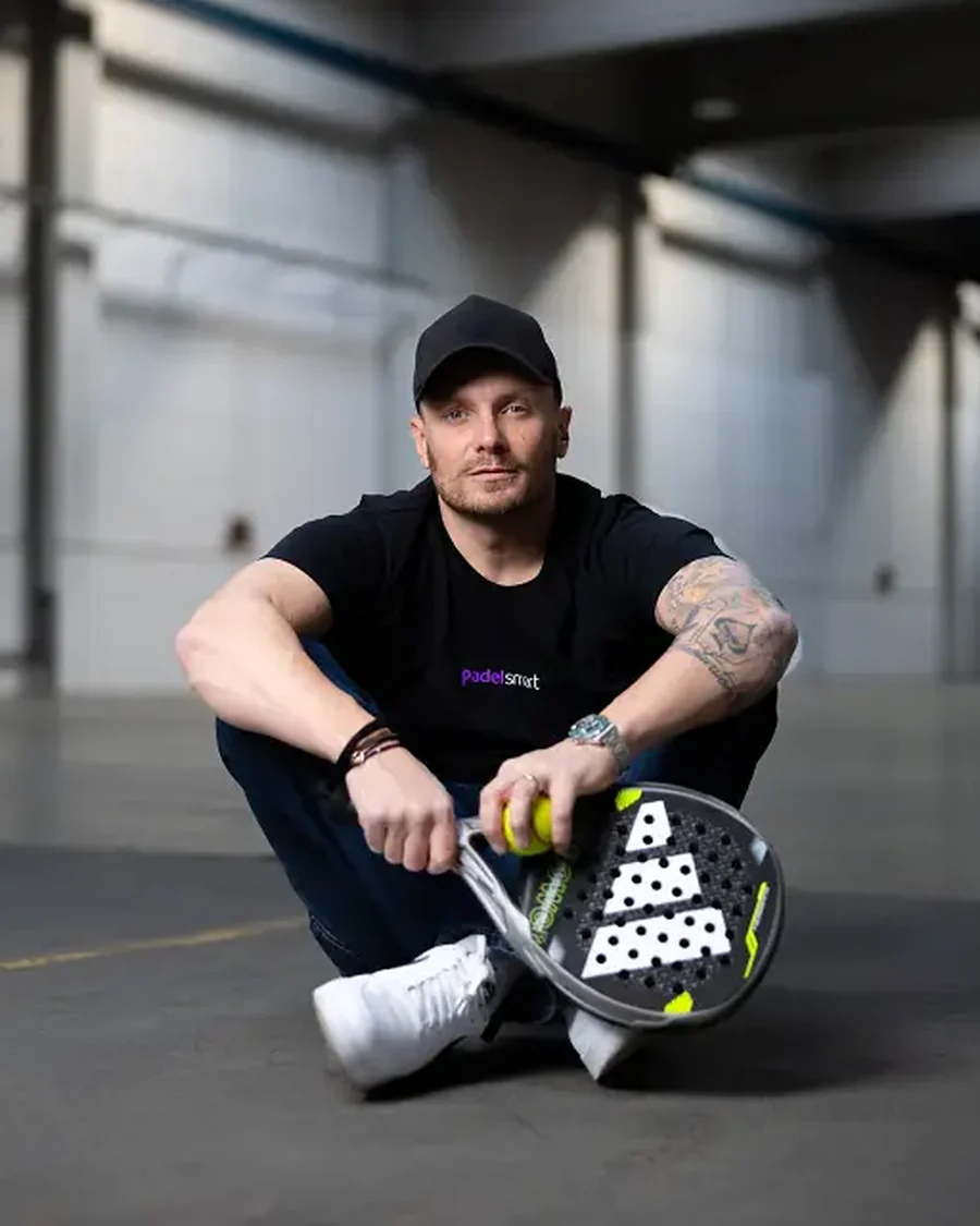 Daniel Fellhauer, Gruender von padelsmart, sitzt mit Schlaeger in einer leeren Halle